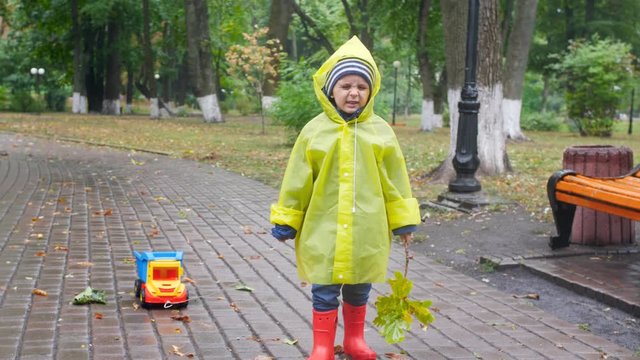 4k video of little boy in yellow plastic raincoat walking in park while raining