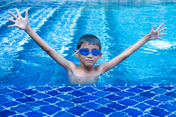 Portrait of asian boy having fun and show up hands in swimming pool and blue refreshing water