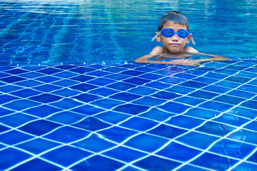 Portrait of asian boy ware a blue glasses and floating at the corner of swimming pool and blue refreshing water