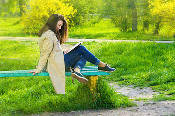 young beautiful happy girl reading a book in the park sitting on a bench. Vintage style