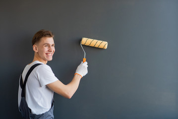 Handsome young smiling worker with paint roller on gray background