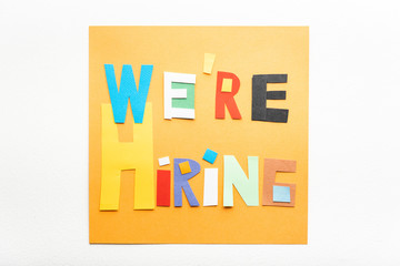 Recruitment concept. We are hiring banner sign made with cut paper on orange on the wall.