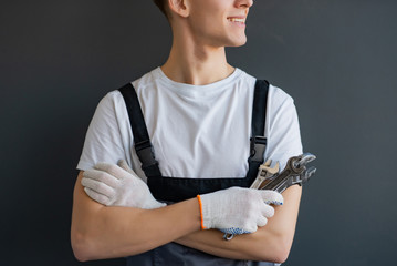 Young Mechanic with crossed arms and wrench standing on gray background