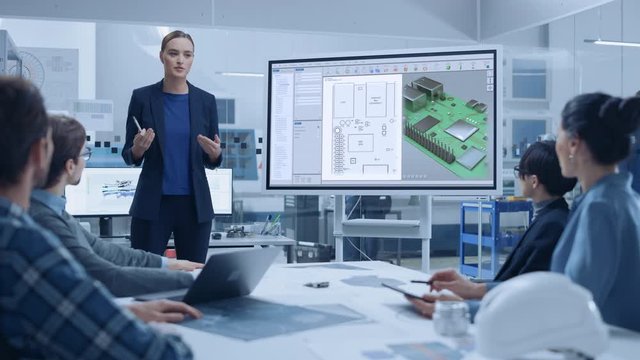 Modern Industrial Factory Meeting: Confident Female Computer Engineer Uses Digital Interactive Whiteboard, Talks to a Group of Engineers, Managers Talks and Shows 3D Printed Circuit Board Concept