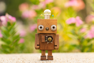 Retro wood robot with light bulb on the head standing in the garden with flower background, nature...