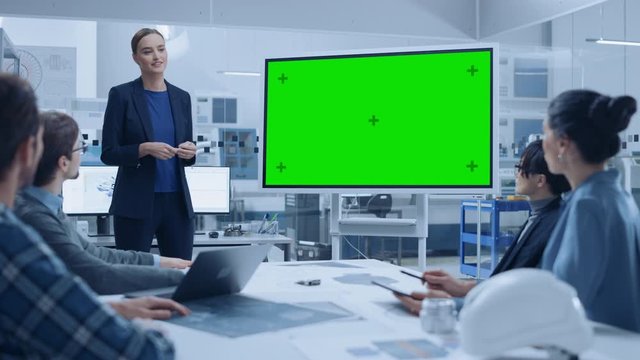Modern Industrial Factory Meeting: Confident Female Engineer Uses Interactive Green Mock-up Screen Whiteboard, Makes Report to a Group of Engineers, Managers 