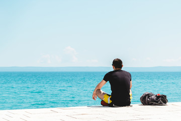 Fototapeta premium young man traveler alone with backpack near him meditating looking into the ocean and enjoying the silence
