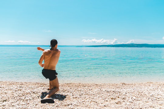 young man traveler with hat on at seaside throwing stones into the ocean. time to relax
