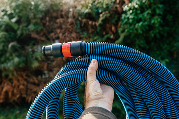 Professional worker male hand holding showing against green garden background new blue anti static vacuum hose for a professional tool vacuum cleaner