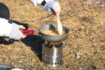 close up hands of woman cooking pasta on wood burner in wild camping