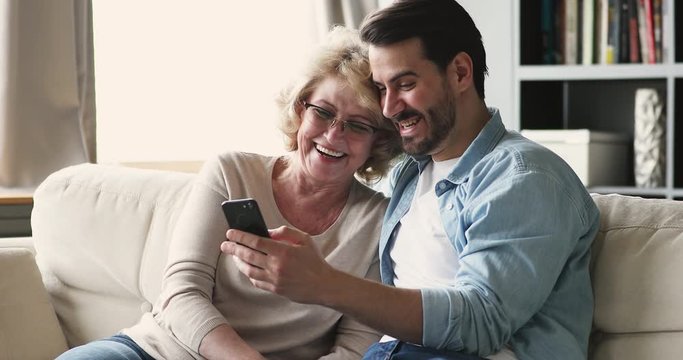 Young son showing funny photos using smartphone with mature mom