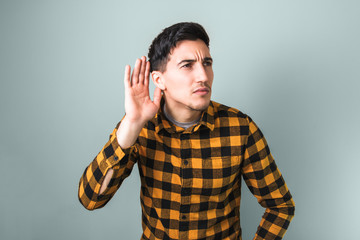 Fototapeta premium handsome young man in trendy yellow shirt trying to hear something on isolated grey background