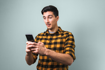 totally surprised man in yellow square shirt looking into the phone on grey background