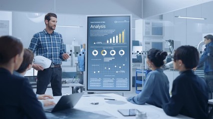 On a Meeting Chief Industrial Engineer Reports to a Group of Specialists, Managers, Uses Digital Whiteboard to Show Statistics with Graphs, Company Productivity Growth. Successful Industrial Factory - Powered by Adobe