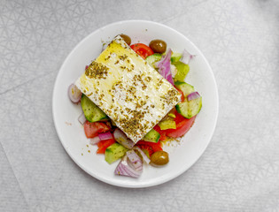 original feta cheese in Greek salad plate, top view close up