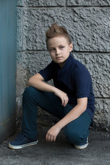 Handsome stylish boy sitting near a wall on the street. The boy has one eye blue, the other green. He is 13 years old.