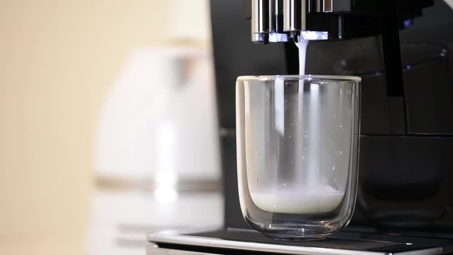 Close-up of the full process of making latte coffee from modern coffee machine, poured in clear glass cup. Coffee machine is making fresh hot latte macchiato with milk foam.