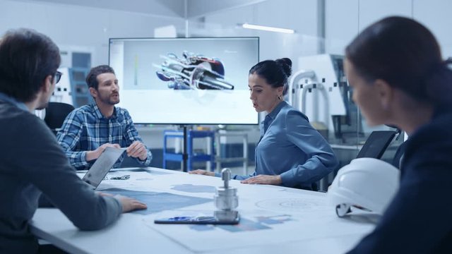 Modern Factory Office Meeting Room: Diverse Team of Engineers, Managers and Investors Talking at Conference Table, Use Interactive TV, Analyze Sustainable Energy Engine Blueprints. High-Tech Facility