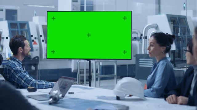Modern Factory Office Meeting Room: Diverse Team of Engineers, Managers and Investors Talking at Conference Table, Watching Interactive TV that shows Green Screen Chroma Key Mock-up