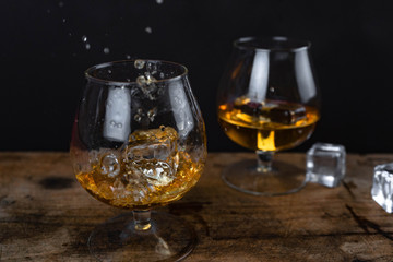 Two whiskey / cognac glasses with ice on a wooden background. Dark backdrop.