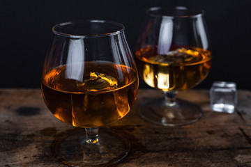 Two whiskey / cognac glasses with ice on a wooden background. Dark backdrop.
