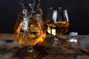 Two whiskey / cognac glasses with ice on a wooden background. Dark backdrop.