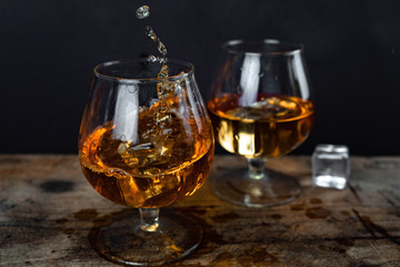 Two whiskey / cognac glasses with ice on a wooden background. Dark backdrop.