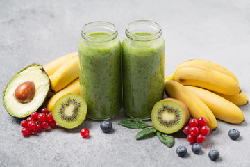 Healthy green smoothie with banana, spinach, berries, avocado and kiwi in a glass bottles