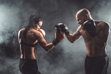 Fototapeta na wymiar Shirtless Woman exercising with trainer at boxing and self defense lesson, studio, dark background. Female and male fight.