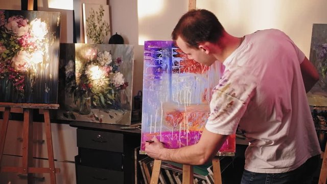 Painting hobby. Creative leisure. Male lefthanded artist adding finishing touch to abstract work.