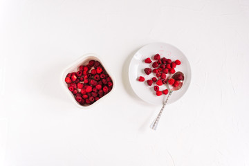 Plate with a silver spoon and a container with raspberries on a white background. Fresh summer berries.