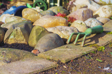 Fototapeta na wymiar Ausschnitt eines frisch erstellten Zier Beet im Garten bei Tageslicht im Frühling. Im Bild befindet sich eine Hand Harke, große Kieselsteine und andere Garten Accessoires.