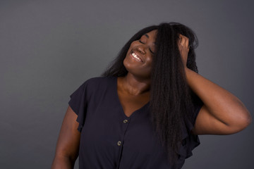 Shot of happy young African American woman with positive smile, has long hair, rejoices having weekend and good rest after hard working exhausting week, isolated on gray wall.