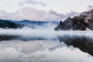 Early morning on a mountain lake. Steam over the water. Blue mountains in the distance.