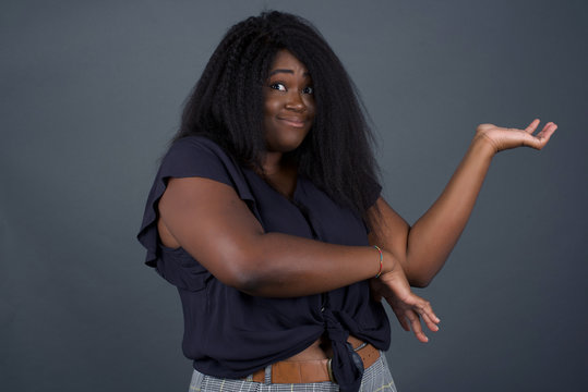 African American girl pointing aside with both hands showing something strange and saying: I don't know what is this. Standing against gray background. Advertisement concept.