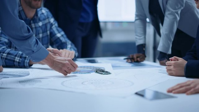 Busy Diverse Team of Computer Engineers and Specialists Gather Around Conference Table, They Discuss Project Drafts and Blueprints, Find Problem Solutions. Office Meeting Room. Slow Motion