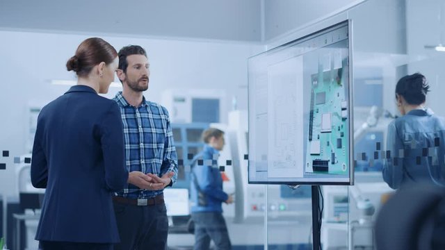 Female Computer Engineer and Male Project Manager Use Digital Interactive Whiteboard That Shows 3D Printed Circuit Board Concept. Developers Find Problem Solution. Modern Factory Meeting Room