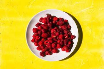 White plate with raspberries on a yellow background with texture. Fresh red berry with vitamins.