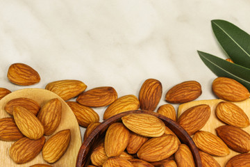 Almond nuts lie in two wooden spoons and in a wooden bowl on white marble