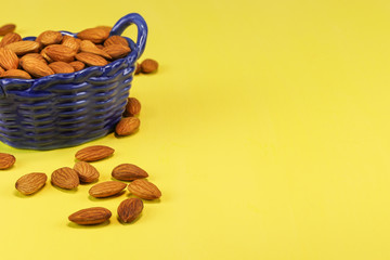 Almond nuts in a blue glass basket and on a yellow surface