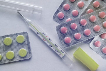 colored pills and thermometer spread out on a light table