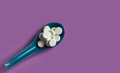medicine pills in a blue spoon on a purple background