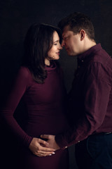 Handsome man is listening to his beautiful pregnant wife's tummy and smiling	