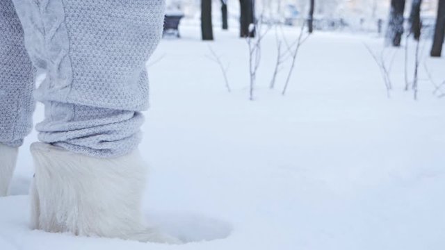 The legs of a young girl are walking in the snow in high boots, felt boots, ugg boots. A snowy winter park. Close-up