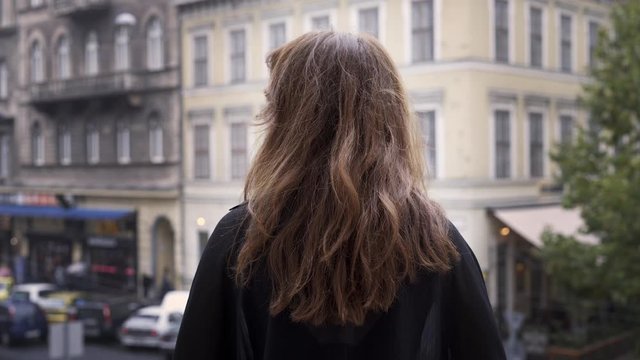 Gimbal shot of woman back standing on the balcony in Budapest, Hungary. Back shot of brunette woman standing on the balcony looking at the houses and road