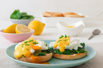 Eggs Florentine, English muffins, grilled ham, poached eggs, Hollandaise sauce, chive herbs, lemon, cup of coffee. White wooden table with breakfast.