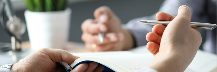 Two clerks discussing business using notebooks and pens close-up