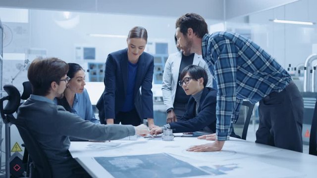 Busy Diverse Team of Engineers and Specialists Gather Around Conference Table, They Discuss Project Drafts and Blueprints, Find Problem Solutions. Industrial Technology Factory / Office Meeting Room