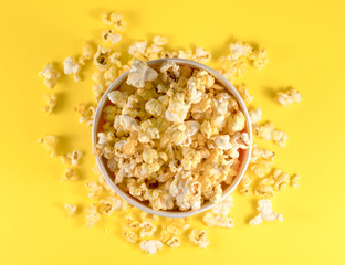 Glass bowl with salted popcorn on yellow background. Top view with copy space. Flat lay.