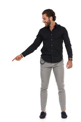 Smiling Man In Gray Trousers, Moccasins And Black Shirt Is Standing And Pointing Down